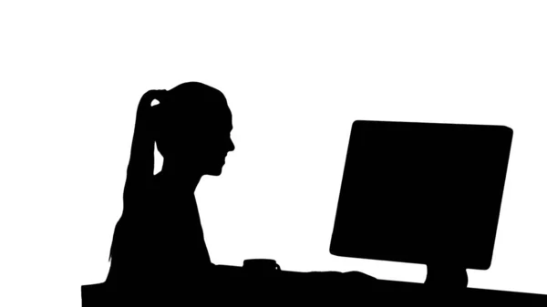 Silhouette Girl ül a számítógép monitor előtt, és néz valami mosolygós. — Stock Fotó