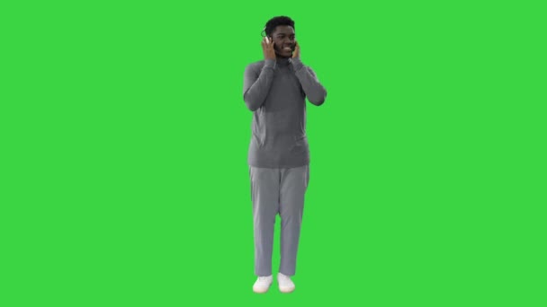 Feliz afro-americano segurando fones de ouvido com as mãos e dançando para a batida de música enquanto sorri para a câmera em uma tela verde, Chroma Key. — Vídeo de Stock
