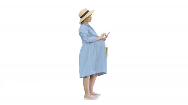 Happy pregnant woman in blue dress and hat using her smartphone on white background. — Stock Video