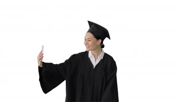 Feliz graduada femenina en mortero haciendo selfie en su teléfono sobre fondo blanco. — Vídeo de stock