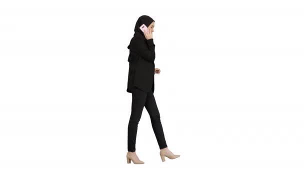 Atractiva mujer musulmana moderna caminando y hablando por teléfono celular sobre fondo blanco. — Vídeos de Stock