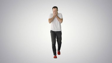 Uykulu erkek beyaz tişörtlü, esniyor ve yürürken gözlerini ovuşturuyor.