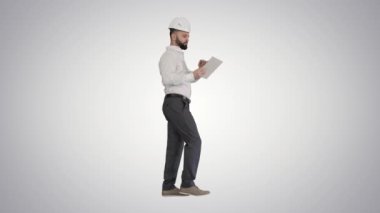 Gradyan arkaplanda yürürken tablet bilgisayar kullanan bir inşaat uzmanı.