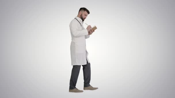 Doktor nebo zdravotník drží pero a notebook hledá nápad při chůzi na gradient pozadí. — Stock video