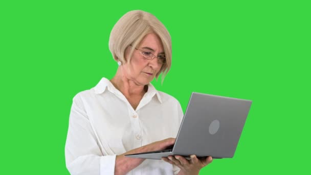 Ernstige volwassen zakenvrouw in bril met behulp van laptop op een groen scherm, Chroma Key. — Stockvideo