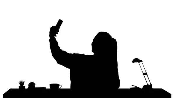 Silhouette Gyönyörű nő csinál egy szelfit a mobiljával ül az asztalnál.. — Stock Fotó