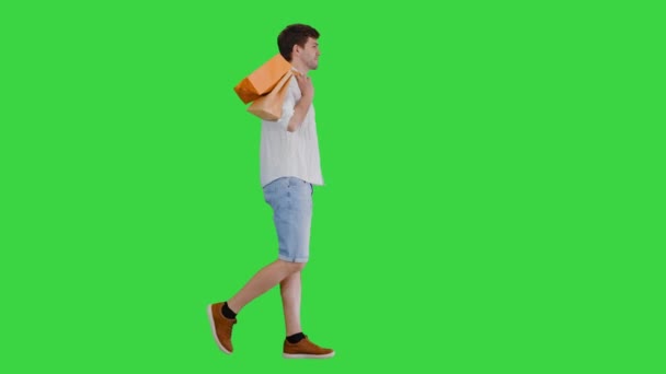 Homem bonito em roupas casuais andando com sacos de compras olhando para a câmera em uma tela verde, Chroma Key. — Vídeo de Stock