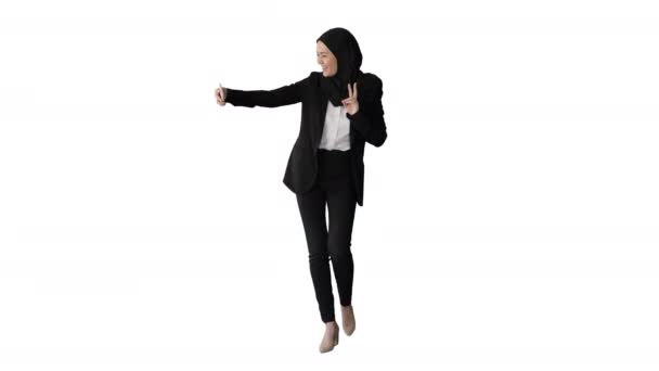 Mujer árabe sonriente en hijab tomando selfies en su teléfono móvil mientras camina sobre fondo blanco. — Vídeos de Stock