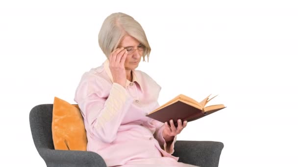 Pensiunan wanita membaca buku duduk di kursi dengan latar belakang putih. — Stok Video