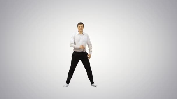 Молодой человек, одетый в белую рубашку и черные брюки прыгают в рамку и начинают танцевать перерыв глядя на камеру на градиентном фоне. — стоковое видео