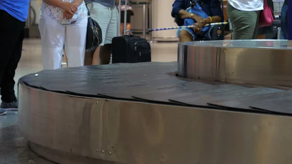 Suitcases on luggage conveyor belt in the baggage claim at airport. People waiting for their luggage.