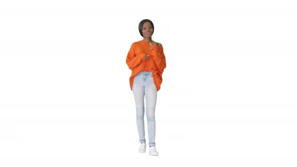 Веселая афроамериканка в ярком свитере и джинсах разговаривает с камерой на белом фоне. — стоковое видео