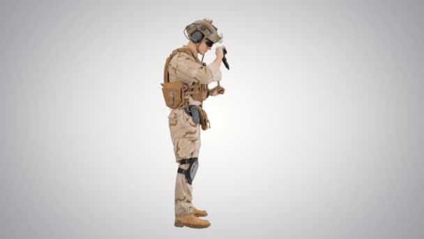 Młody człowiek w mundurze wojskowym sprawdza rewolwer na gradientowym tle.. — Wideo stockowe