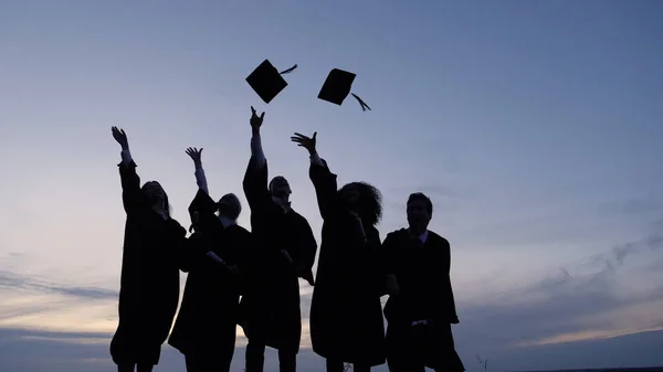Sylwetka absolwentów rzucających czapki w powietrze. — Zdjęcie stockowe