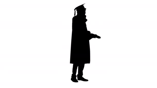 シルエット男はガウンを着て卒業し、電話で会話をしているmortarboard. — ストック動画