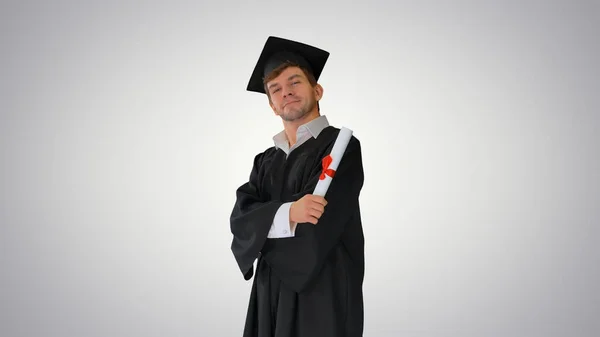 Mezuniyet elbisesi içinde gururlu bir erkek öğrenci diplomasıyla poz veriyor. — Stok fotoğraf