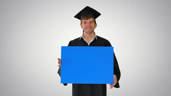 Smiling graduate male in mortarboard holding blank sign on gradi — Stock Photo, Image