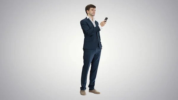 Серьезный бизнесмен смотрит на свой телефон на градиентном фоне. — стоковое фото