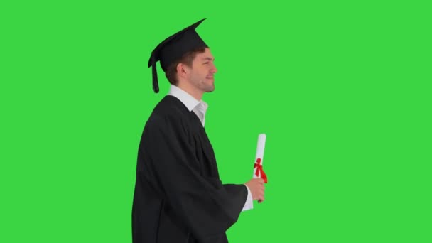 穿着毕业典礼礼服、拿着毕业证书在绿色屏幕上走着的男同学笑着，铬钥匙. — 图库视频影像