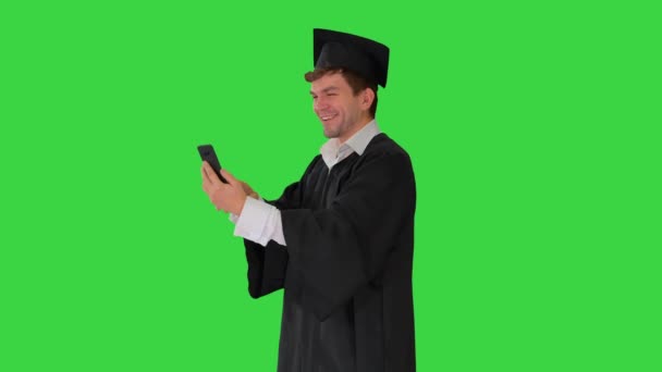 穿着毕业礼服的男生在绿色屏幕上的手机上通过视频显示校园，Chroma Key. — 图库视频影像