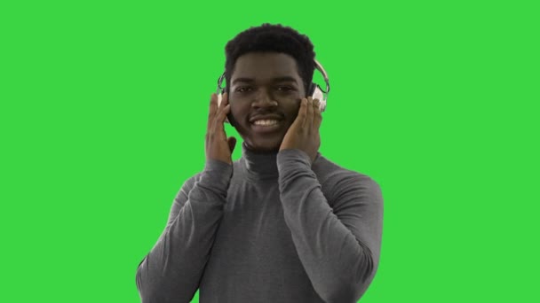 Heureux afro-américain tenant des écouteurs avec ses mains et dansant au rythme de la musique tout en souriant à la caméra sur un écran vert, Chroma Key. — Video