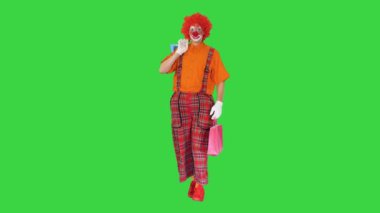 Yeşil ekranda alışveriş torbalarıyla yürüyen komik palyaço, Chroma Key.