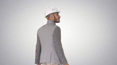 Miğferli ve çantalı mühendis eğimli arka planda yürüyor