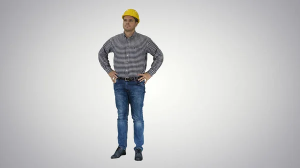 完璧なよく構築されたオブジェクトを見て黄色のヘルメットに笑みを浮かべて建設労働者グラデーションの背景に腰の手. — ストック写真