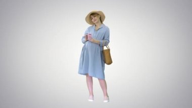 Mavi elbiseli ve şapkalı mutlu hamile kadın gradyan arka planda akıllı telefonunu kullanıyor..