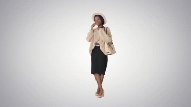 Örgü ve şapka giymiş gülümseyen Afro-Amerikan kadın telefonuyla grafiksel arka planda konuşuyor..