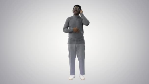 Glimlachende Afro-Amerikaanse man in hoofdtelefoon en verplaatsen naar de muziek ritme op gradiënt achtergrond. — Stockvideo