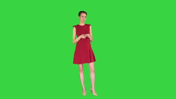 Joven mujer atractiva feliz en el vestido rojo mensajes de texto en el teléfono en una pantalla verde, Chroma Key. — Vídeo de stock