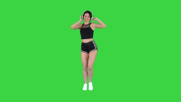 Jovem mulher esportiva feliz ouvindo música em fones de ouvido e dançando em uma tela verde, Chroma Key. — Vídeo de Stock