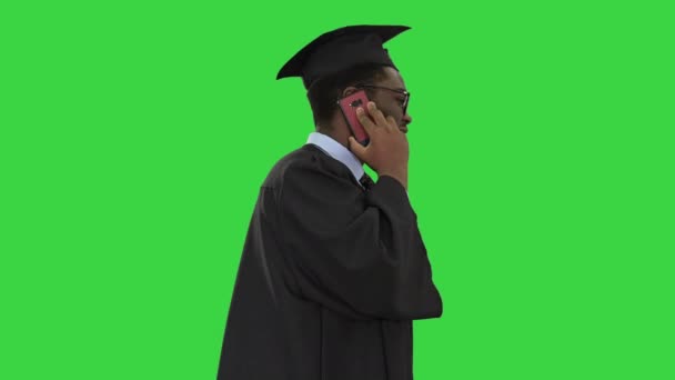 Lächelnder afrikanisch-amerikanischer Student im Abschlussgewand, der auf einem Green Screen telefoniert, Chroma Key. — Stockvideo