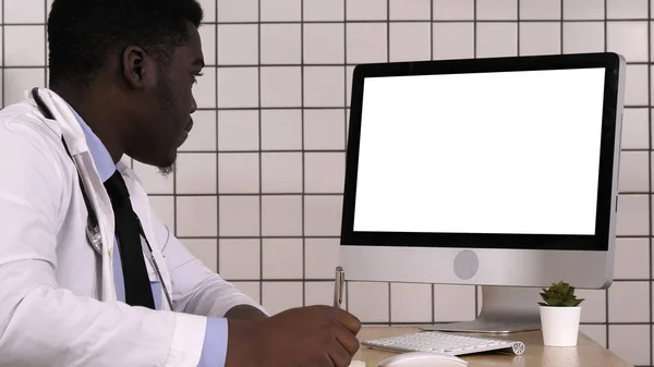 Νεαρός Αφρικανός γιατρός με εργαστηριακή ποδιά κάθεται στο γραφείο του και μιλάει. — Φωτογραφία Αρχείου