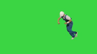 Sarı kasketli genç inşaat işçisi el dönüşü yapıyor kameraya bakıyor ve yeşil ekran, Chroma Key 'de yürüyor..