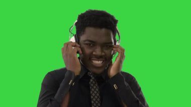 Afrika kökenli Amerikalı bir adam iki eliyle kulaklık tutuyor ve yeşil ekranda gülümseyerek kameraya bakarken müzik dinliyor, Chroma Key.