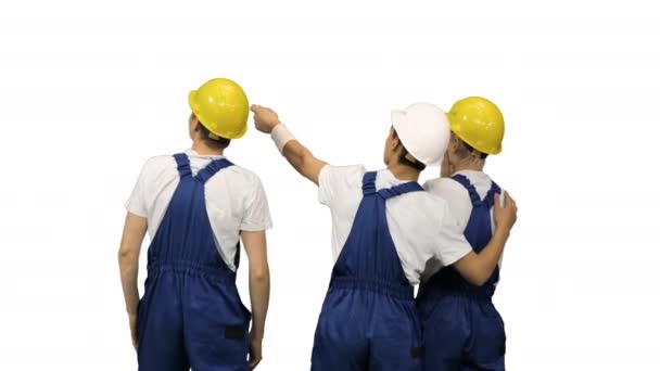 Tre operai di sesso maschile in hardhats guardando il cantiere e discutendo con le spalle alla macchina fotografica su sfondo bianco. — Video Stock