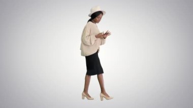Örgü ve şapkalı şık Afro-Amerikan kadın. Grafik arka planda yürürken telefonunu kullanıyor..