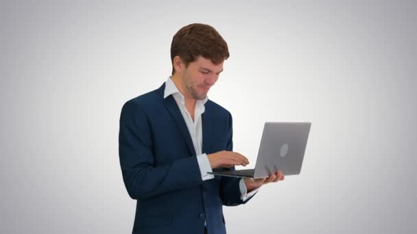 Sonriente joven hombre de negocios utilizando el ordenador portátil, mientras que de pie en el fondo gradiente. — Vídeos de Stock
