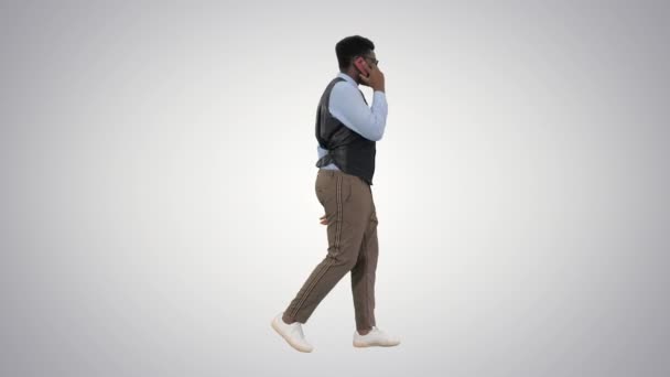 Sonriente joven hombre de negocios afroamericano hablando por teléfono mientras camina sobre el fondo gradiente. — Vídeos de Stock