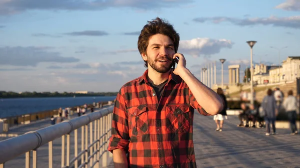 Guapo estudiante masculino caminando al aire libre y hablando en el teléfono móvil. —  Fotos de Stock