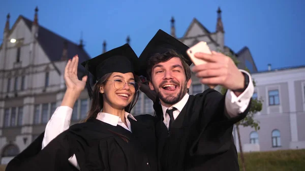 Gelukkige mannelijke en vrouwelijke afgestudeerde studenten nemen van een selfie. — Stockfoto