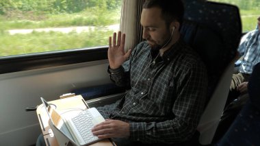 Kulaklık takan genç bir uzman trende dizüstü bilgisayar kullanarak işvereniyle görüntülü konuşma yapıyor..