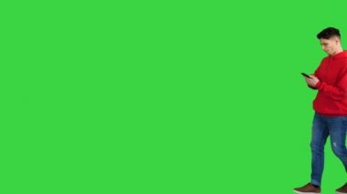 Yakışıklı, sıradan bir adam, akıllı telefonuyla müzik dinliyor ve yeşil ekranda yürürken dans ediyor, Chroma Key.