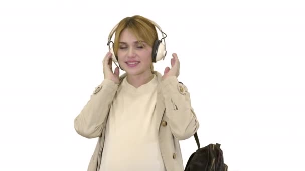 Ung attraktiv gravid kvinde lytter til musik i hovedtelefoner søger at kamera på hvid baggrund. – Stock-video