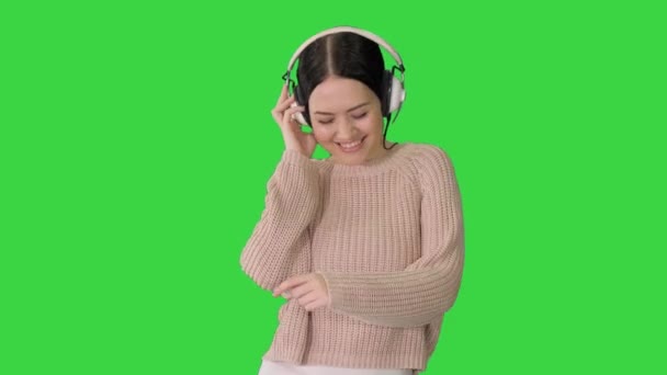 Mosolygó nő fülhallgatóval séta és tánc a zene egy zöld képernyőn, Chroma Key. — Stock videók
