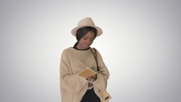 Bella donna afroamericana in maglia maglione e cappello scrittura nel suo blocco note su sfondo sfumato. — Video Stock