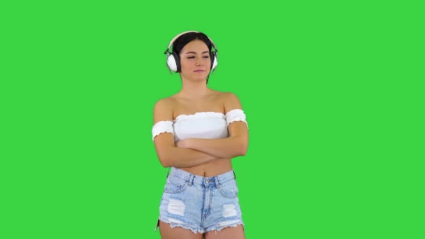 Mujer hispana joven que usa auriculares cara seria pensando en una pantalla verde, Chroma Key. — Vídeo de stock