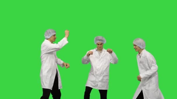 Three male doctors in white robes and protective caps doing funny celebration dance on a Green Screen, Chroma Key. — Stock Video